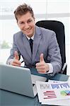 Happy businessman at his desk giving thumbs up