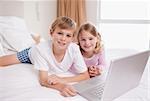 Siblings using a laptop in a bedroom