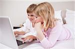 Smiling children using a laptop in a bedroom