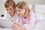 Siblings using a tablet computer in a bedroom