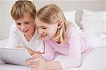 Smiling siblings using a tablet computer in a bedroom