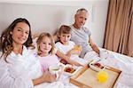 Smiling family having breakfast in a bedroom while looking at the camera