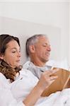 Portrait of a woman reading a book while her husband is reading a newspaper in their bedroom