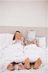 Portrait of woman reading a book while her companion is reading a newspaper in their bedroom