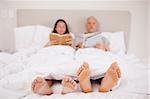 Woman reading a book while her companion is reading the news in their bedroom