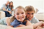 Happy siblings posing on a carpet with their parents on the background in a living room