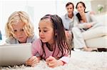 Cute siblings using a tablet computer while their parents are in the background in a living room