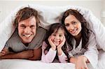 Parents lying under a duvet with their daughter in their bedroom