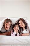 Portrait of parents lying under a duvet with their daughter in their bedroom