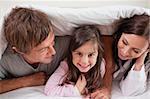Cheerful family lying under a duvet in a bedroom