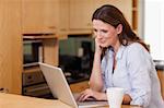 Smiling woman in the kitchen looking at her laptop