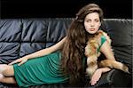 sophisticated elegant woman laying on a black sofa with hair style and wearing a green dress and a tail fur looking in camera