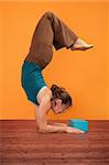 Woman practices Pincha Mayurasana over orange background