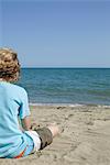 Boy sitting on beach, looking at sea