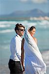Bride and groom standing on beach, looking at view