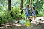 Children running toward bucket and butterfly net in woods