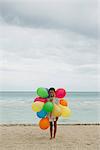 Girl with bunch of colorful balloons on beach