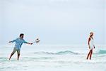 Couple standing in sea, woman walking away from man as he holds out a bouquet