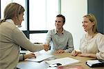 Couple shaking hands with businesswoman in office