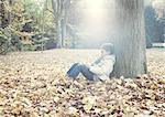 Boy sitting under tree in autumn leaves, portrait