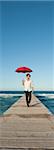 Junger Mann zu Fuß auf Pier mit Regenschirm