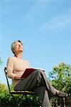 Senior woman sitting outdoors with book, enjoying warmth of sun