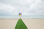 Girl standing on artificial turf on beach with bunch of balloons, rear view