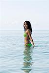 Young woman in bikini standing waist deep in water, portrait