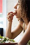 Jeune femme aux cheveux bouclés manger salade, vue latérale