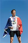 Male athlete being honored on podium, wrapped in French flag