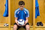 Young soccer player looking down at soccer in hands, portrait