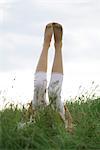 Girl lyingon back in tall grass with legs raised in the air