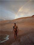 USA, Utah, Lake Powell, Young woman wearing bikini and walking, rainbow in the background