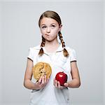 Studio shot of girl (10-11) holding cookie and red apple