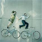 USA, Utah, Salt Lake City, Couple lying holding hands and lying on pavements with their bikes