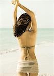 Woman standing on beach with arms up, rear view