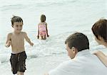 Family at the beach, boy running out of water towards parents