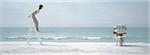 Woman standing on ladder on beach, man reading newspaper