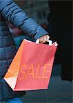 Person holding out shopping bag with "sale" printed on side