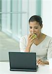 Woman eating apple and using laptop