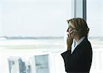 Woman using cell phone in airport, looking out window