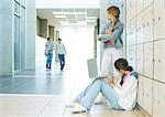 Two high school girls by lockers, watching teen boys approaching