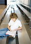 Teen boy reading book on bleachers