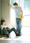 Teen boy with basketball approaching second boy studying in hallway