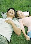 Jeune couple couché dans l'herbe, tête à tête, rire