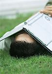 Man lying in grass with laptop covering face