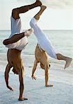 Two men turning cartwheels on beach