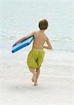 Boy running toward sea carrying body board