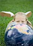 Girl lying on grass with globe, looking at camera