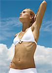Femme portant des bikini, qui s'étend avec la main derrière la tête, le ciel en arrière-plan